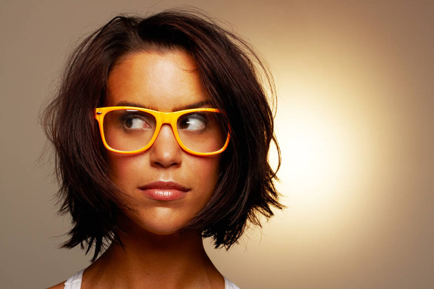 Mírně zmatený.... Oříznutý záběr atraktivní mladé ženy nosí brýle na hnědém pozadí. - Fotografie, Obrázek