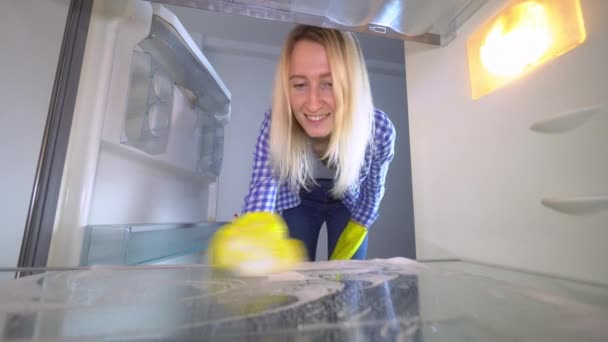 A nő kinyitja a hűtő ajtaját, elmossa és kitakarítja belül, és mosolyog. - Felvétel, videó