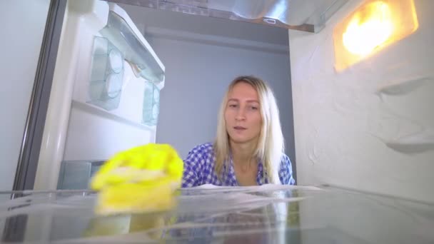Tyytymätön ja ärtynyt nainen pesee ja puhdistaa jääkaapin sisällä - Materiaali, video