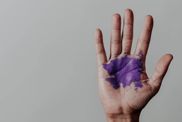 la mano levantada de un hombre con algunas manchas de pintura púrpura, sobre un fondo gris con un poco de espacio en blanco a la izquierda - Foto, imagen