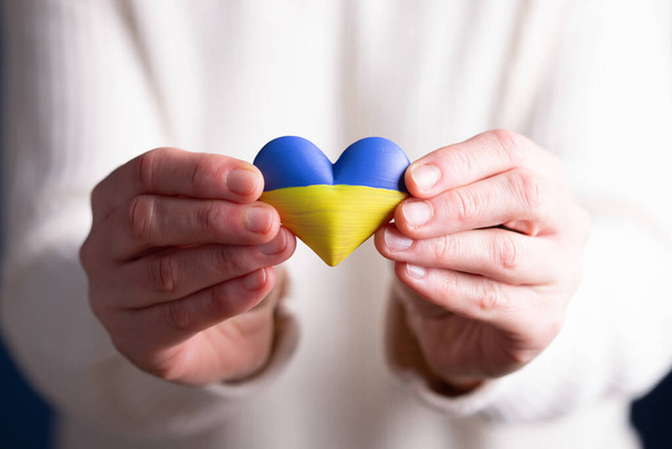 Heart shaped flag of Ukraine in female hands. The concept of solidarity with the citizens of Ukraine. - Fotó, kép