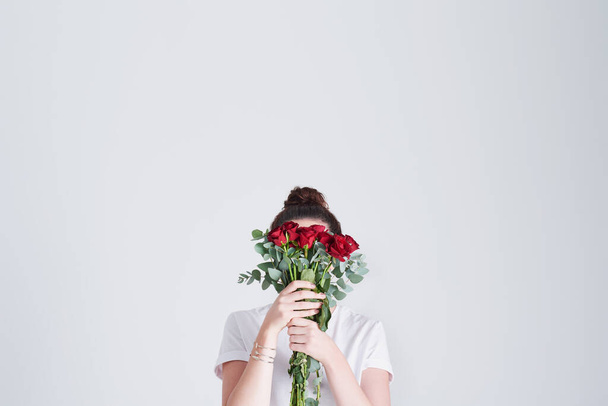 Láska vášnivě jako rudá růže. Studio záběr nerozpoznatelné ženy zakrývající její tvář s květinami na šedém pozadí. - Fotografie, Obrázek
