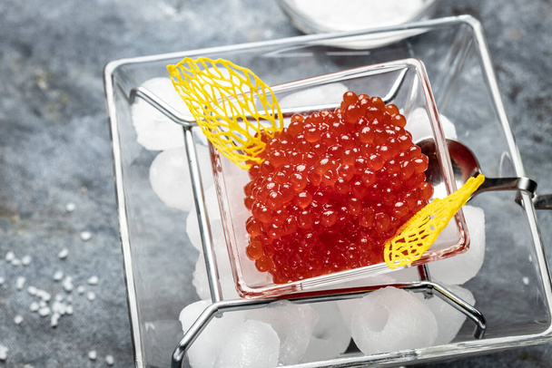 Red Caviar in a spoon. Caviar in bowl over black background. Close-up salmon caviar. Delicatessen. Gourmet food. Texture of caviar. Seafood. - Фото, изображение