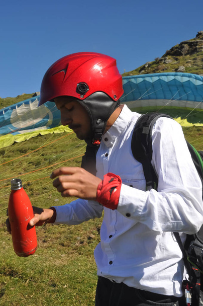 Ένα νεαρό αρσενικό τουρίστα κρατώντας μπουκάλι για πόσιμο νερό πριν από τη λήψη αλεξίπτωτο πλαγιάς πτήση στο βουνό της Himachal Pradesh  - Φωτογραφία, εικόνα