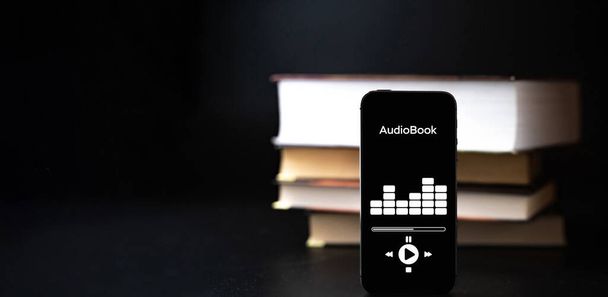 Edukacja audiobooka. Ekran telefonu z aplikacją książki audio na papierowych książek czarne tło. Nauka online, koncepcja szkoły domowej - Zdjęcie, obraz