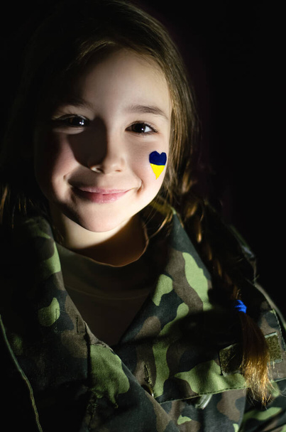 улыбающийся ребенок с раскрашенным украинским флагом на щеке, изолированный от черного  - Фото, изображение
