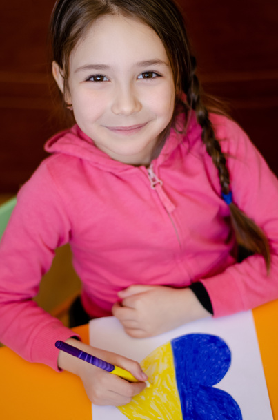 Hochwinkelansicht des fröhlichen Kindes, das Herz mit ukrainischen Flaggenfarben auf Papier zeichnet - Foto, Bild