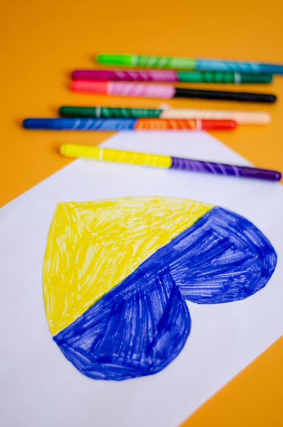 high angle view of modern felt pens near paper with drawn heart and ukrainian flag on yellow  - Photo, Image
