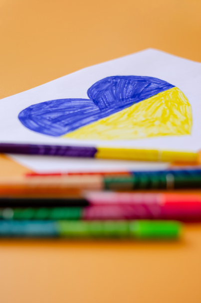 blurred felt pens near paper with drawn heart and ukrainian flag isolated on yellow  - Photo, Image
