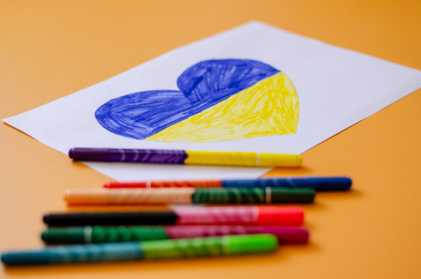 blurred felt pens near paper with drawn ukrainian flag in heart on yellow  - Zdjęcie, obraz