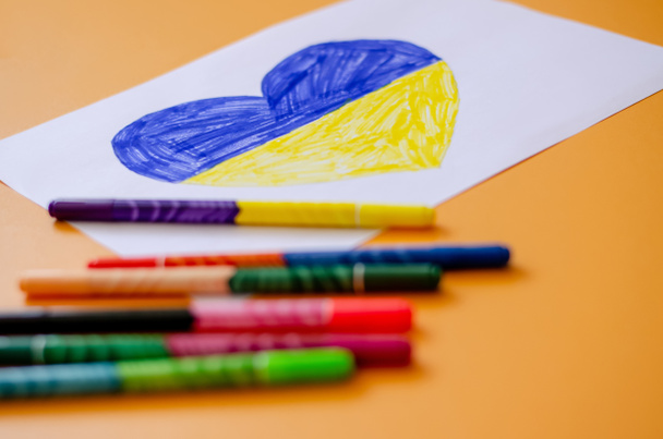 felt pens and paper with drawn ukrainian flag in heart on yellow  - Photo, Image