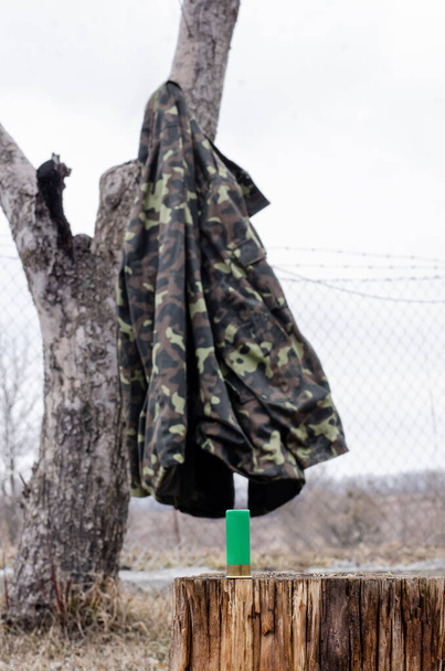 дробовик на деревянном пне рядом с камуфляжной курткой в лесу - Фото, изображение