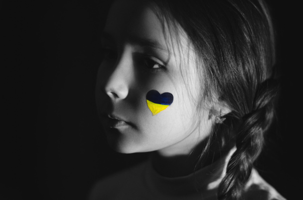 Монохромное фото расстроенной девушки с нарисованным украинским флагом на щеке, изолированным на черном  - Фото, изображение