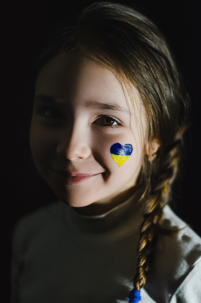 χαρούμενο κορίτσι με ζωγραφισμένη ουκρανική σημαία στο μάγουλο απομονωμένο σε μαύρο  - Φωτογραφία, εικόνα