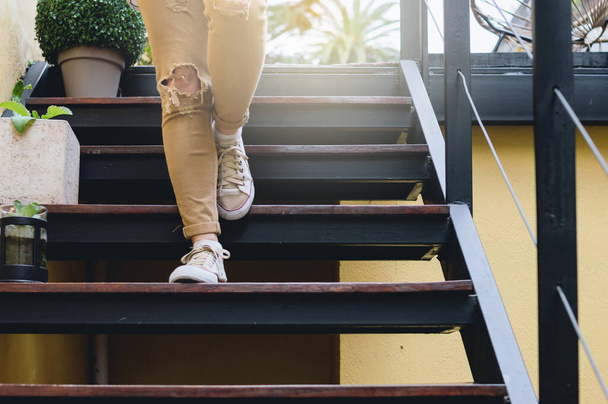 detalle en las piernas y los pies de una joven con pantalones de color mostaza bajando las escaleras al aire libre. - Foto, Imagen