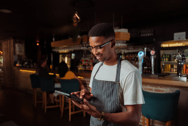 アフリカ系アメリカ人のウエイターは、デジタルタブレットを保持レストランで働く - 写真・画像