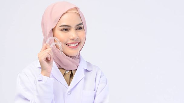 A muslim female dentist holding invisalign braces over white background studio, dental healthcare and Orthodontic concept - Photo, image