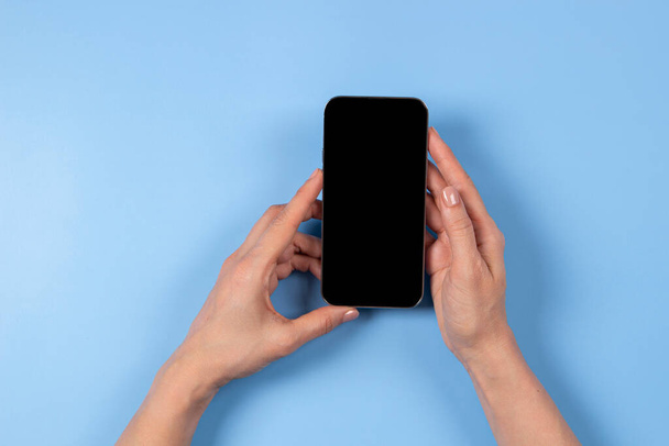 Female hand holding smartphone on light blue background - Fotoğraf, Görsel
