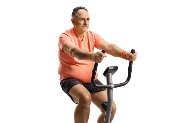 Mature man exercising on a stationary bike isolated on white background - Photo, image