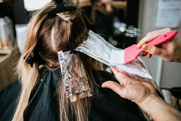 Hairdresser is dyeing female hair, making hair highlights to his client with a foil.  - Fotografie, Obrázek