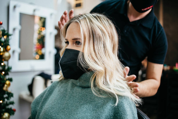 Beautiful hairstyle of woman after dyeing hair and making highlights in hair salon. She is wearing protective face mask as protection against virus pandemic. - Φωτογραφία, εικόνα