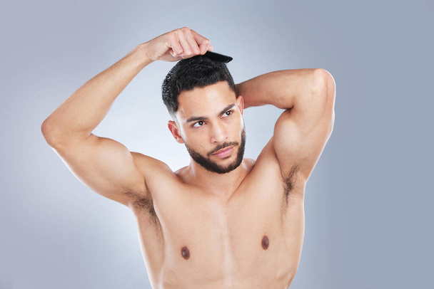 Looking good takes attention to detail. Studio shot of a handsome young man combing his hair against a grey background. - Foto, Bild
