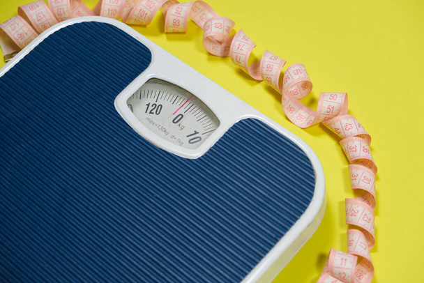 Floor blue scales and centimeter measuring tape on a yellow background, top view. The concept of weight loss and weight control. - Photo, Image