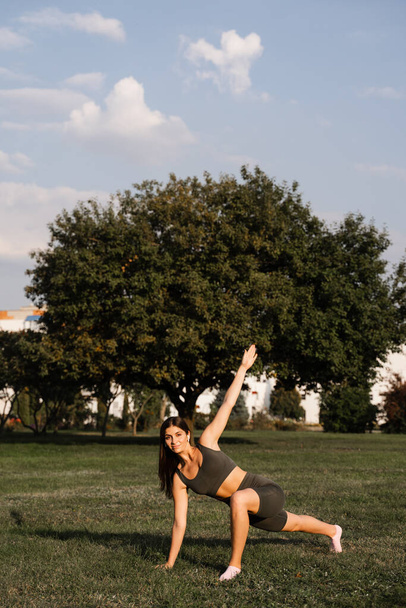 Fit girl does warm-up and stretching exercises in green park. Sports lifestyle - Photo, Image