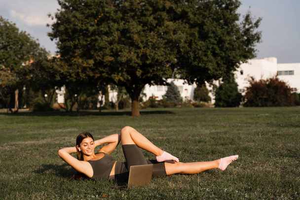Formation en ligne avec ordinateur portable dans le parc vert. Active fit girl fait séance de fitness en plein air - Photo, image