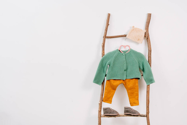 Детская одежда и обувь на деревянной натуральной лестнице на белом фоне с пустым местом для текста. - Фото, изображение