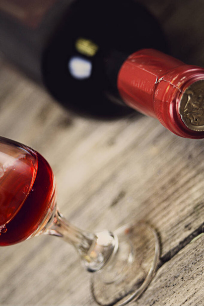Een fles wijn in horizontale positie en een glas wijn op een ruw houtoppervlak - Foto, afbeelding