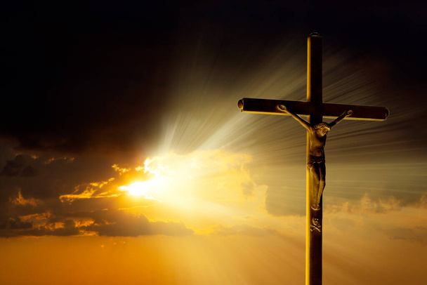Kříž ukřižování stojí na pozadí působivé zlaté oblohy se zářivými paprsky pronikajícími mraky - Fotografie, Obrázek