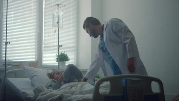 Γιατρός ελέγχει λίγο ασθενή στο θάλαμο του νοσοκομείου. Άρρωστο κορίτσι αγκαλιάζει βελούδινο παιχνίδι - Πλάνα, βίντεο