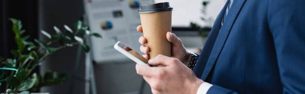 vista recortada de economista con café para ir de mensajería en el teléfono móvil en la oficina, pancarta - Foto, Imagen
