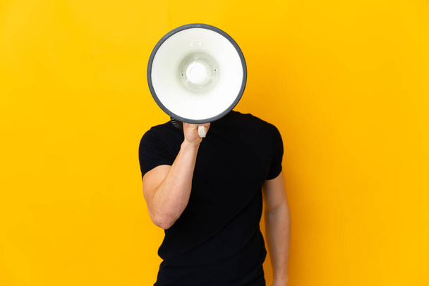 Young caucasian man isolated on yellow background shouting through a megaphone to announce something - Φωτογραφία, εικόνα