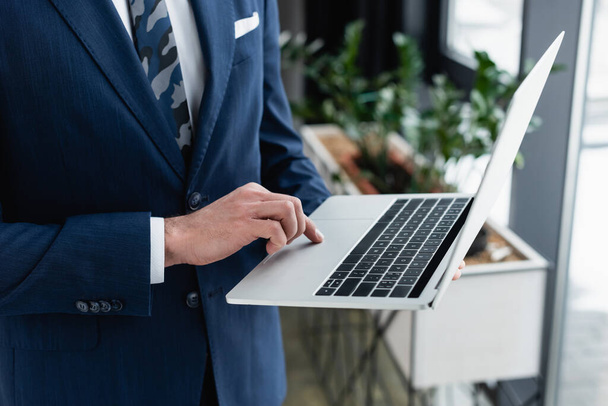 cropped view of businessman using laptop while standing in office - Foto, imagen