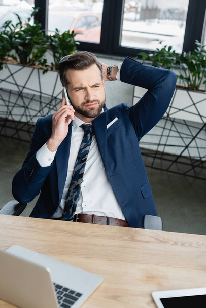 thoughtful businessman looking away while talking on smartphone in office - Photo, Image