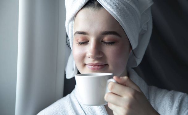 Egy fiatal nő törülközővel a fején, egy csésze kávéval reggel.. - Fotó, kép