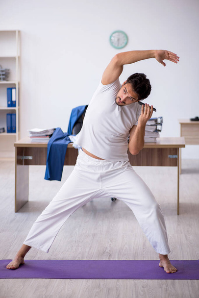 Joven empleado masculino haciendo ejercicios deportivos en la oficina - Foto, imagen