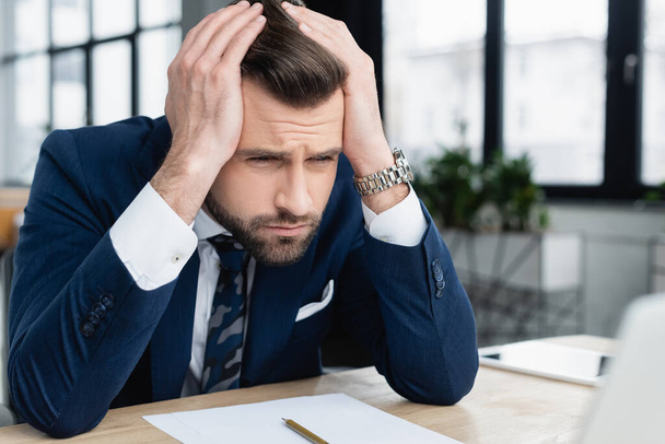 displeased businessman holding hands on head while sitting at workplace - Valokuva, kuva