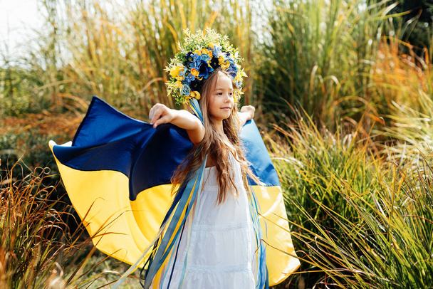 Ukrainian child girl in embroidered shirt vyshyvanka with yellow and blue flag of Ukraine in field. - Fotó, kép