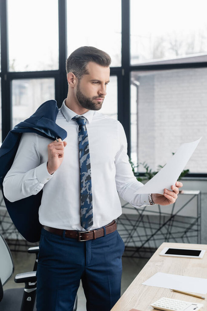 econoom in wit shirt op zoek naar papier tijdens het staan in het kantoor - Foto, afbeelding
