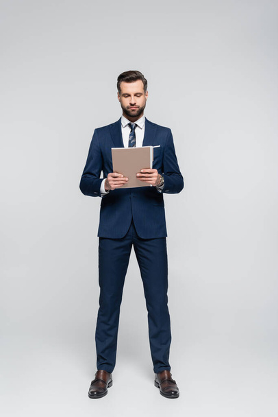 full length view of businessman in blue suit holding folder on grey - Фото, изображение