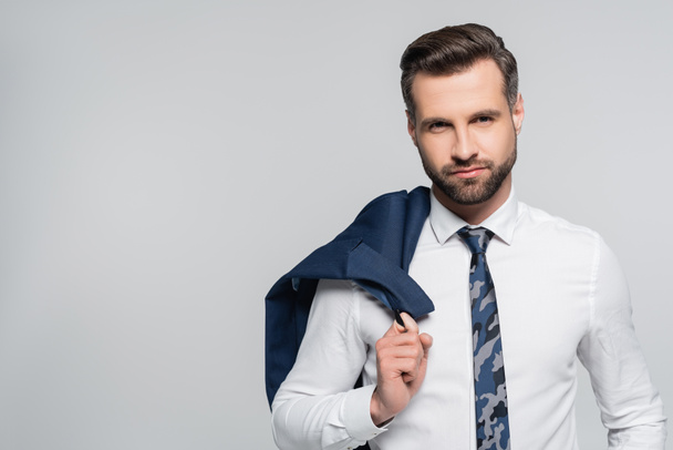 επιχειρηματίας με λευκό πουκάμισο κρατώντας σακάκι και κοιτάζοντας κάμερα απομονωμένη σε γκρι - Φωτογραφία, εικόνα