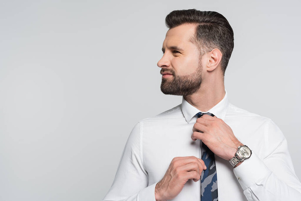 brunette economist in white shirt adjusting tie while looking away isolated on grey - Foto, afbeelding