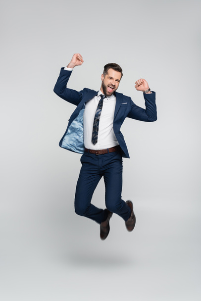 excited businessman showing triumph gesture while levitating on grey - Photo, Image