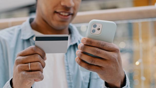 Afrykański, troskliwy klient człowiek wprowadza bankowe dane karty kredytowej w telefonie komórkowym płaci zakup wybierając towary online decyduje płatności internetowe transfery finansowe wirtualne pieniądze netto aplikacja - Zdjęcie, obraz
