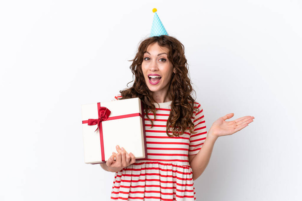 Young woman with curly hair holding present isolated on white background with shocked facial expression - Foto, Imagem