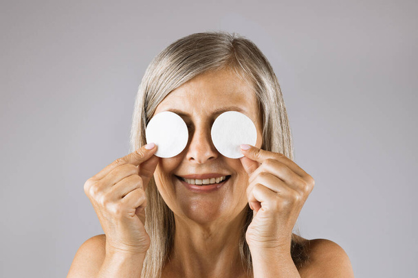 Mature woman covering eyes with two cotton pads - Foto, Imagen