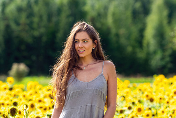portrait of a beautiful brunette woman in a linen country style dress in a sunflower field - Foto, Imagem